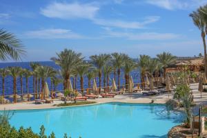 - une piscine avec des chaises longues, des palmiers et l'océan dans l'établissement The Grand Hotel Sharm El Sheikh, à Charm el-Cheikh