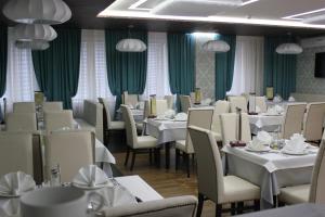 um restaurante com mesas e cadeiras brancas e cortinas verdes em Hotel Rossiya em Noyabrsk