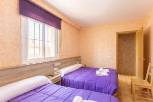two beds in a room with purple sheets and a window at Los Montero in Villamanrique de Tajo