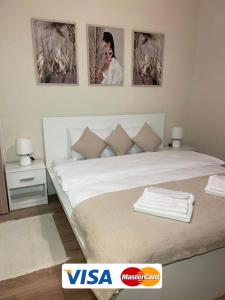 una camera da letto con un grande letto bianco con immagini appese al muro di Airport Alexandra Apartments a Surčin
