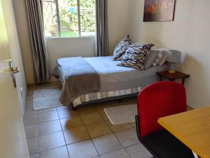 1 dormitorio con 1 cama con silla roja y ventana en Thandanani Serene place, en Pietermaritzburg