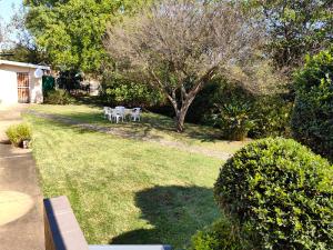 un patio con dos sillas blancas y un árbol en Thandanani Serene place, en Pietermaritzburg