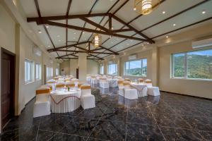 a banquet hall with white tables and chairs and windows at juSTa Birding Resort & Spa - Best Dhauladhar View Resort in Dharamshala