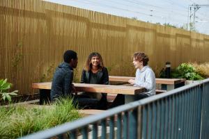 Un groupe de trois personnes assises à une table de pique-nique dans l'établissement For Students Only Private Bedrooms with Shared Kitchen, Studios and Apartments at Canvas Walthamstow in London, à Londres