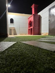 a building with a red tower next to a grass yard at شاليهات توليب in Al Falt