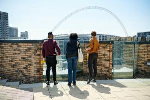 tres personas de pie en una cornisa mirando hacia una ciudad en Private Bedrooms with Shared Kitchen, Studios and Apartments at Canvas Wembley in London en Londres