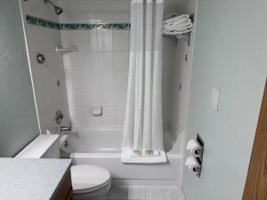 a white bathroom with a toilet and a bath tub at Promenade Inn & Suites Oceanfront in Seaside