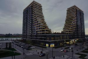 dois edifícios altos ao lado de um parque de estacionamento com carros em Belgrade Waterfront Comfortable Apartment em Belgrado