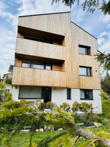 a building with a wooden facade with trees in the foreground at NORDIC Apartamente Păltiniș in Păltiniş