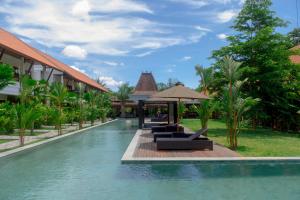 a pool at a resort with lounge chairs and an umbrella at Griya Shanti Suites in Sanur