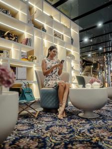 Uma mulher sentada numa cadeira numa loja a olhar para o telemóvel. em Golden Sands Boutique Hotel-Dubai Creek em Dubai
