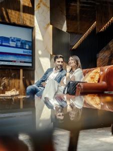 Ein Mann und eine Frau sitzen auf einer Couch vor einem Fernseher in der Unterkunft Golden Sands Boutique Hotel-Dubai Creek in Dubai