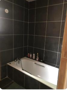 a bath tub in a bathroom with black tiles at Ty case péi in Saint-Aignan