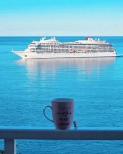 a cup of coffee sitting on a railing with a cruise ship at Indy's Beach Apartments in Dubrovnik