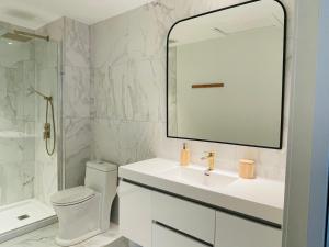 La salle de bains blanche est pourvue d'un lavabo et d'un miroir. dans l'établissement Pavillon Neuf Baie de Tadoussac Clim Parking - 1 chambre, à Tadoussac
