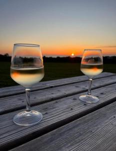 two glasses of wine sitting on a wooden table with the sunset at Camping Les Ronds Duval face aux îles anglo-normandes in Les Moitiers-dʼAllonne