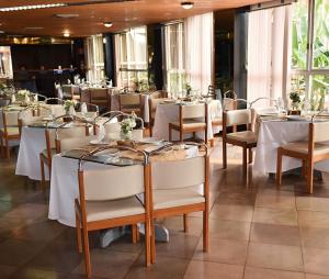 uma sala de jantar com mesas e cadeiras brancas em Harbor Querência Hotel em Cascavel