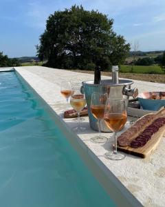 una mesa con copas de vino y aperitivos junto a una piscina en Maison Cabet, en Castelnavet