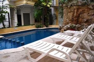 a group of white lounge chairs next to a swimming pool at Hotel Maya Turquesa in Playa del Carmen