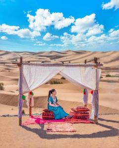 uma mulher sentada sob um dossel no deserto em Deep Desert Camp em Merzouga