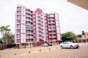 een groot rood gebouw met auto's geparkeerd voor het bij Gail Homes Naalya - One bedroom luxury apartment in Kampala