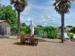 einen Tisch und Stühle mit einem Sonnenschirm und Palmen in der Unterkunft Maison 3 chambres Longeville in Longeville-sur-Mer