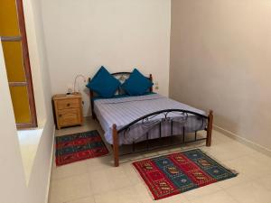 a bedroom with a bed with blue pillows and two rugs at Riad Dar Tazoulte in Agdz
