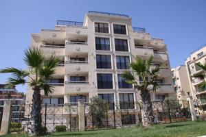 a building with palm trees in front of it at Golden Dunes Primorsko Apartments in Primorsko