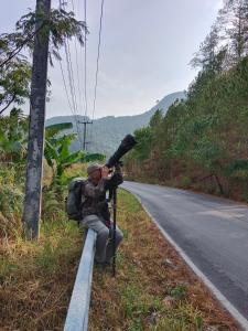 a man sitting on the side of a road with a camera at Rangbondoi - Birdwatching Included 