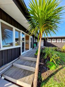 a wooden porch with a palm tree in front of a house at Peace and Aroha Mangawhai - Apartment in Mangawhai