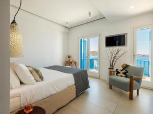 a bedroom with a bed and a chair and windows at Bluetopia Suites in Mýkonos City