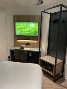 OZO Hotels Antares Airport في هوفدوربْ: غرفة نوم بسرير ومكتب مع تلفزيون