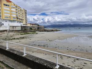 a beach with a white railing next to the ocean at Apartamento playa Carrabuxeira (Sanxenxo) in Sanxenxo