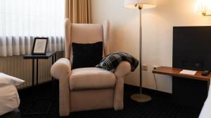 a room with a chair and a lamp and a television at Parkhotel Cloppenburg in Cloppenburg