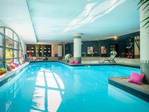 a large swimming pool with blue water in a building at Hotel Parc Beaumont & Spa Pau - MGallery in Pau