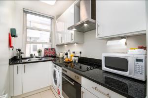 cocina con armarios blancos y microondas en Selfridges Parkside Haven - 2 Bedroom Apartment, en Londres