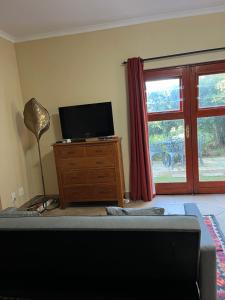 a living room with a tv on a wooden dresser with a window at Wine Cottage by the Sea in Helderberg