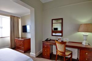 Habitación de hotel con escritorio, cama y espejo en The Balmoral en Durban