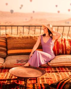 烏奇薩爾的住宿－Ages in Cappadocia，坐在沙发上的身着紫色连衣裙和帽子的女人