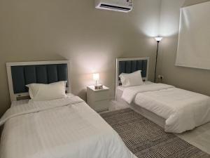 Elegant Apartment in Al-Narjis شقة أنيقة بثلاث غرف وصالة تسجيل ذاتي في الرياض: سريرين في غرفة ذات أغطية ووسائد بيضاء