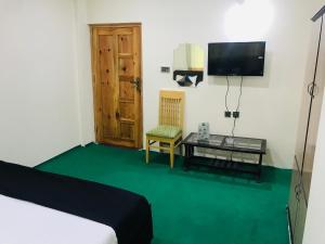 a room with a bed and a table and a television at Mulberry Continental Hotel Skardu in Skardu
