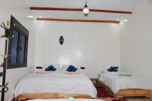 2 Betten in einem Zimmer mit weißen Wänden und blauen Kissen in der Unterkunft Hotel AZUL Todra Gorges in Tinghir