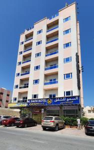 Al Smou Hotel Apartments - MAHA HOSPITALITY GROUP في عجمان: مبنى ابيض كبير فيه سيارات تقف امامه