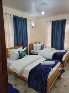 two beds in a room with blue curtains at Gloria House in Nairobi