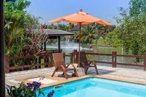 a pool with two chairs and an umbrella next to a table and chairs at Baankwaeom Boutique Homestay Amphawa in Ban Wat Bot