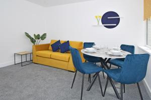 a dining room with a yellow couch and a table with blue chairs at Sapphire Apartments by YourStays - Luxury 2 Bedroom Apartments in Crewe in Crewe