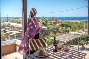 una mujer parada en un balcón con una mesa con copas de vino en Xasteria en Elafonisi 