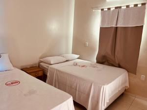 duas camas num pequeno quarto com lençóis brancos em POUSADA E AGENCIA CLEDIO TURISMO em Barreirinhas