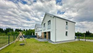 a white house with a playground in a yard at Domy wakacyjne WELLE in Kołczewo