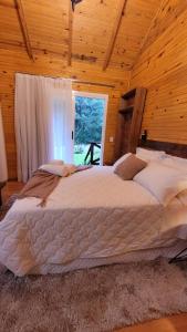 Cama grande en habitación de madera con ventana en Valle Das Águas en Urubici